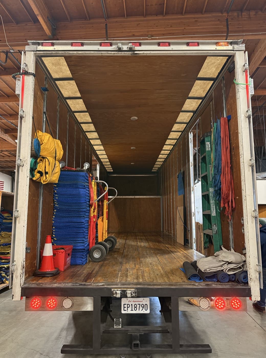 Inside an SVM box truck at the warehouse: quilted pads stacked, two hand trucks strapped to the wall, lifting straps hung by the door, and floor runners rolled at the tail